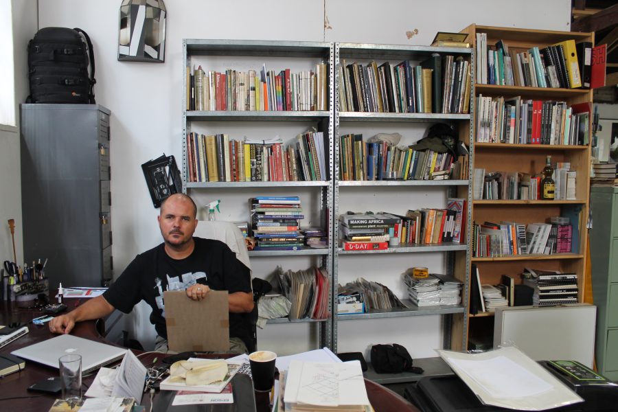 Hobbs at his desk, clasping a packaged set of Buildings, bombs, bunkers and clouds.